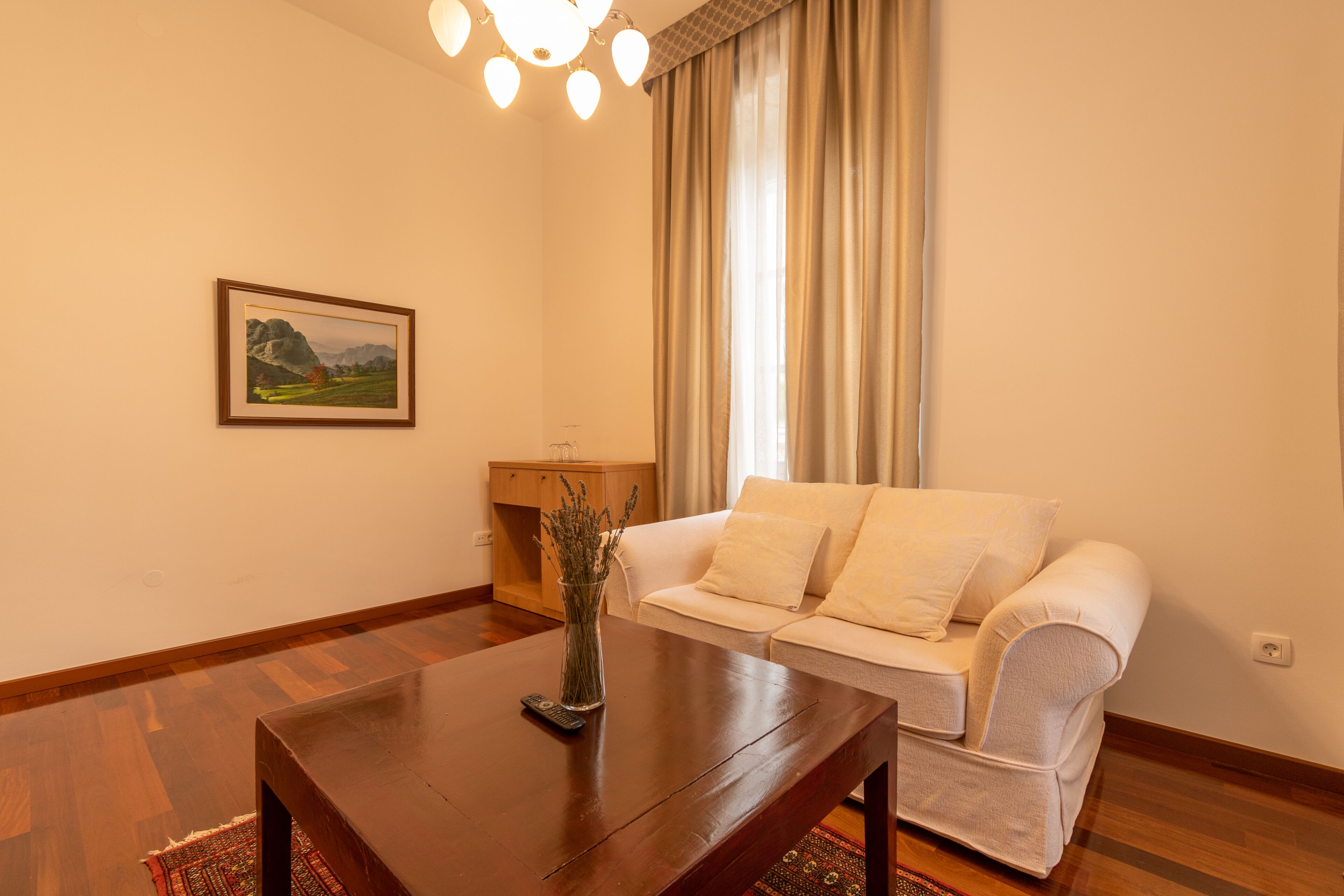 Un salon avec une table basse en bois, un canapé blanc, un tableau au mur et une fenêtre avec des rideaux.