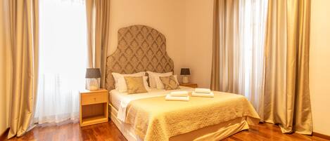 A neatly made bed with a headboard, two bedside tables with lamps, and a wooden floor.