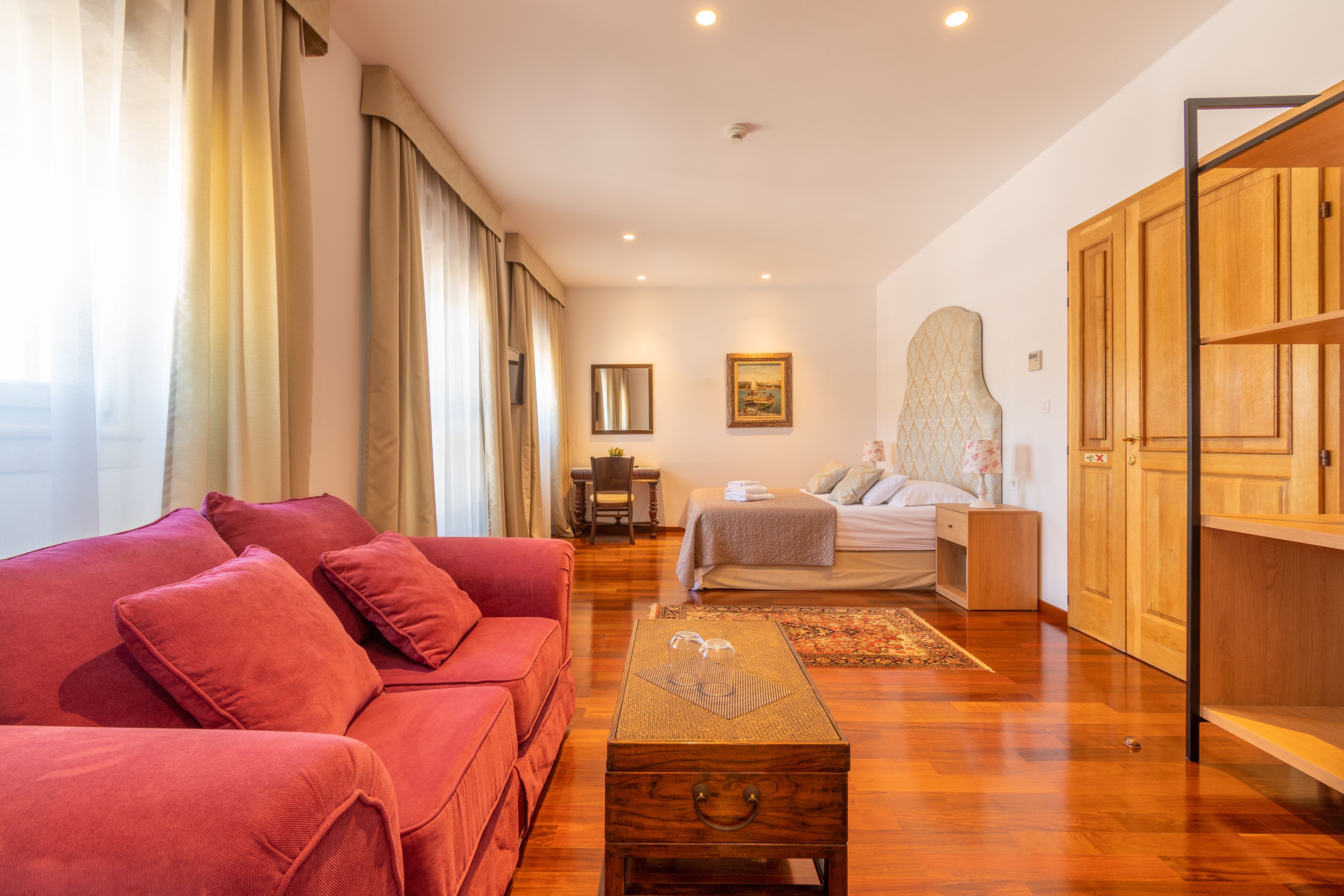 A modern living room with a red sofa, a wooden coffee table, and a bed with a headboard.