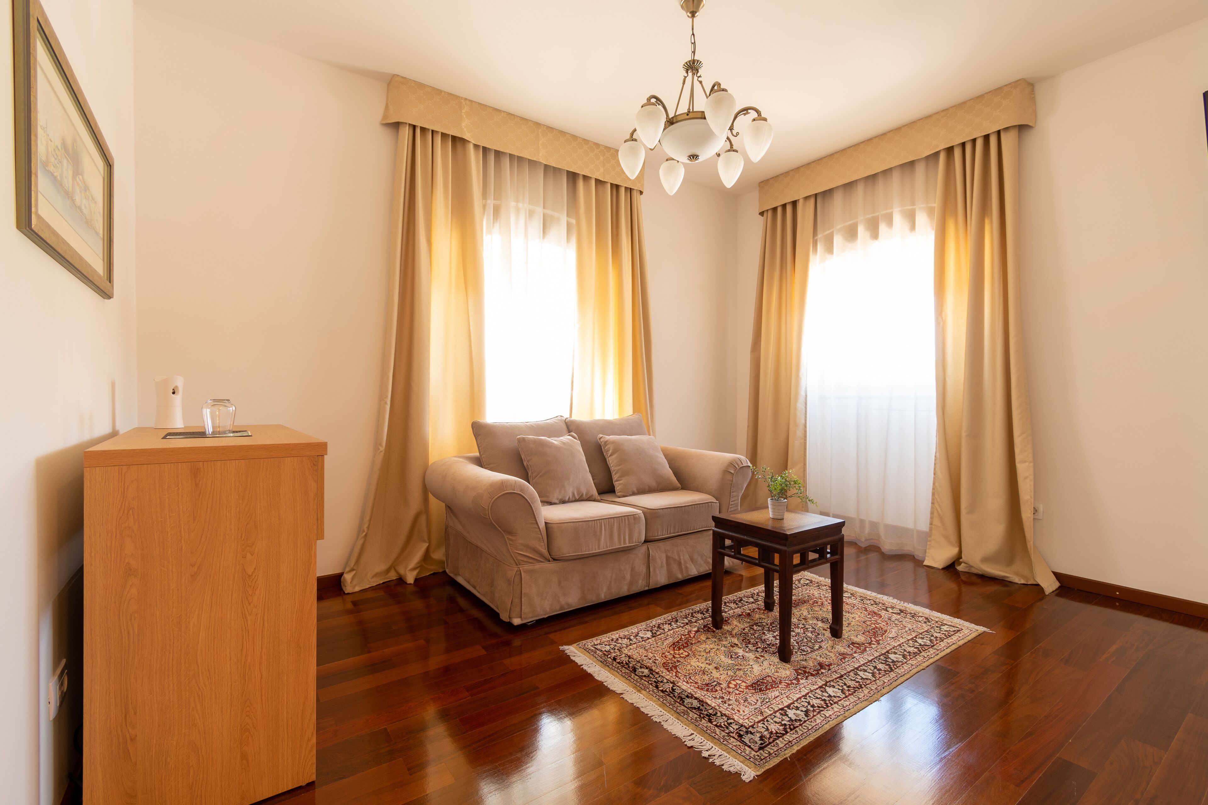 A living room with a beige sofa, a wooden side table, and a patterned rug.