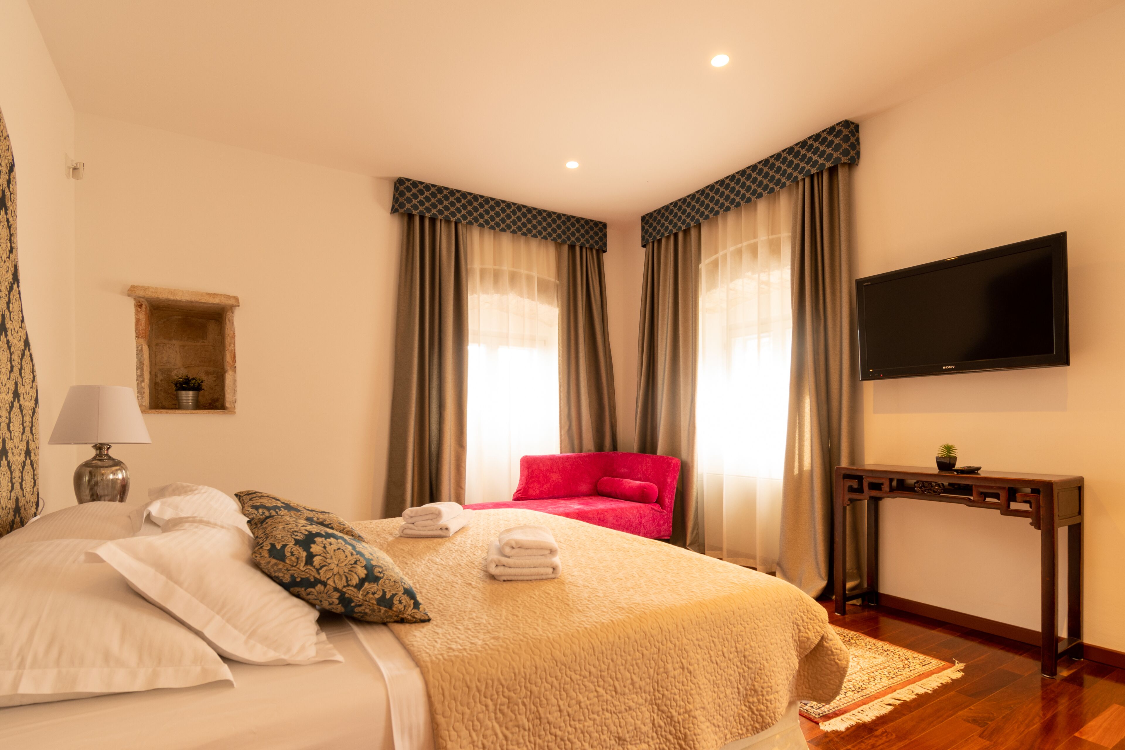 Een hotelkamer met een bed, een rode stoel, een televisie en een console tafel.