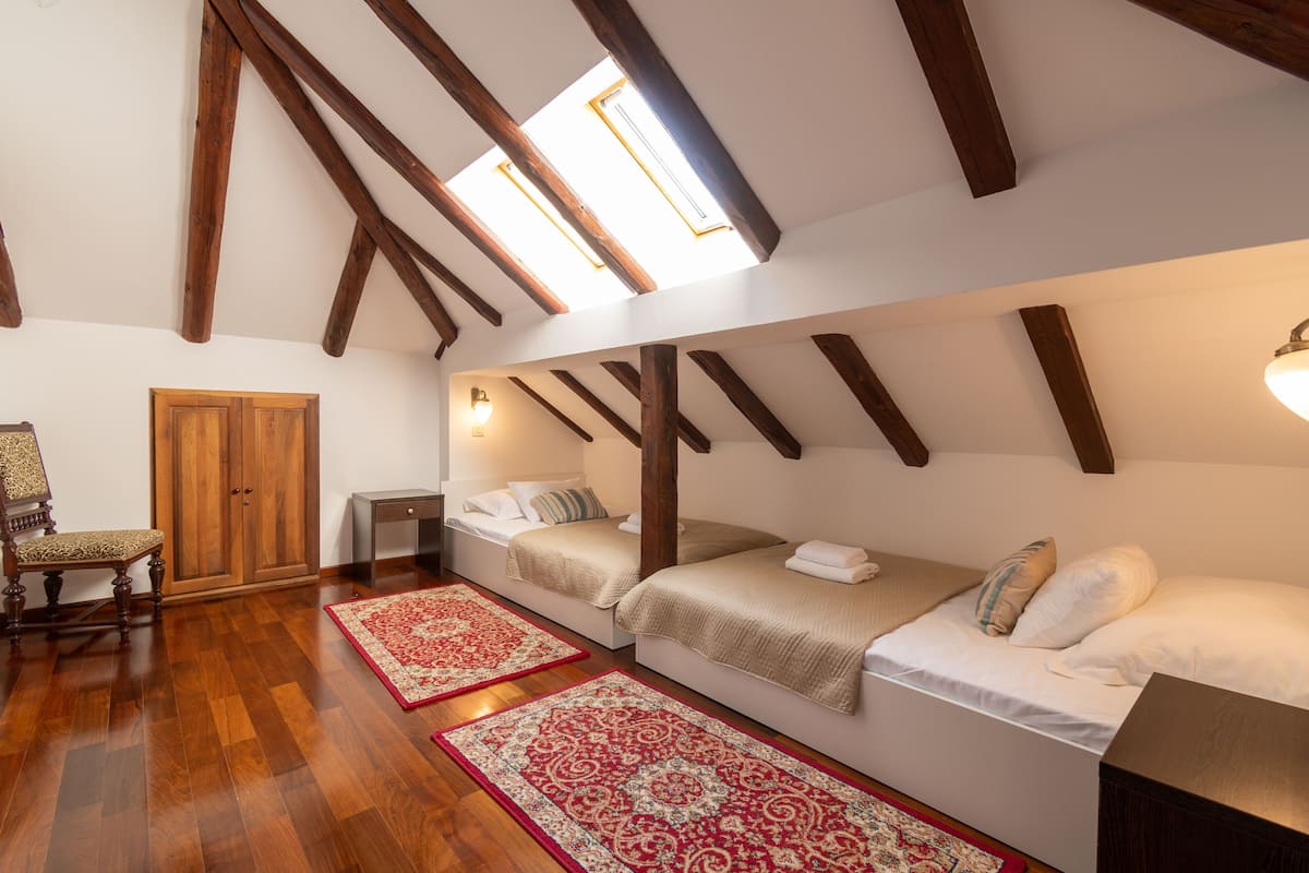 Ein Schlafzimmer mit zwei Betten, Holzbalken, einem Dachfenster, einem Kleiderschrank und einem Sessel.