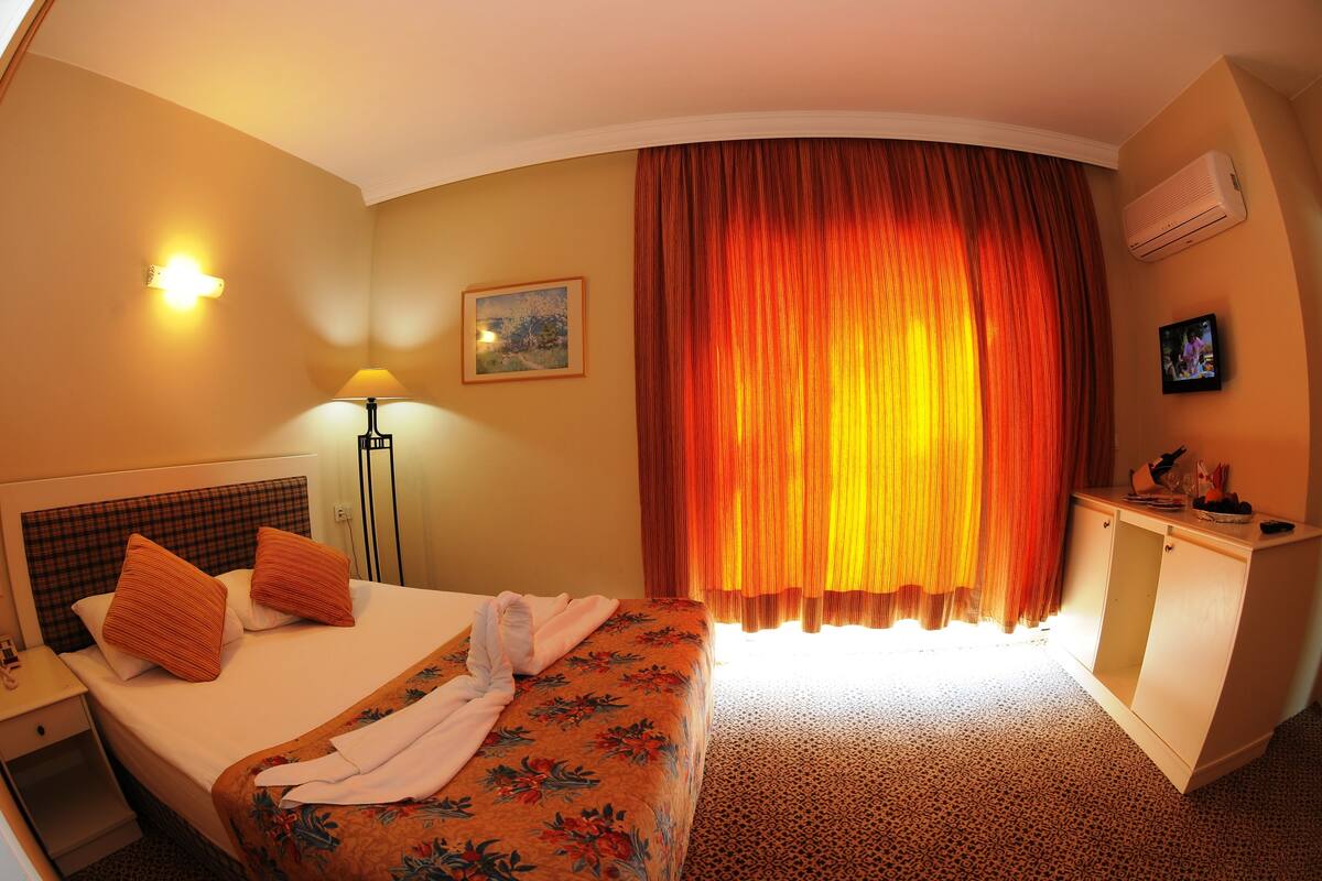 Ein Hotelzimmer mit einem Bett, einem Schreibtisch, einer Lampe, einem Gemälde und einem Fenster mit Vorhängen.