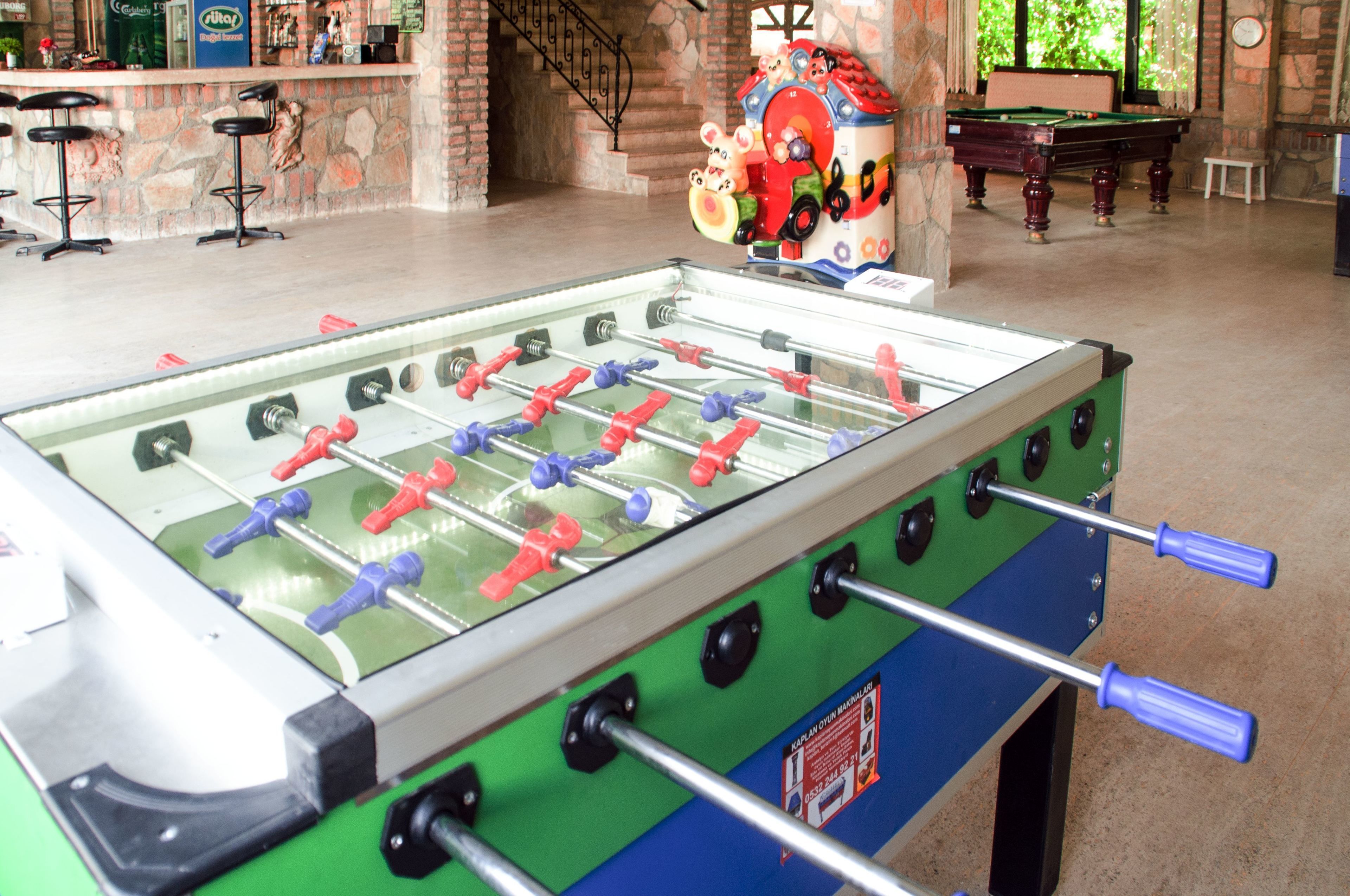 A foosball table in a room with a pool table, bar stools, and a decorative house model.