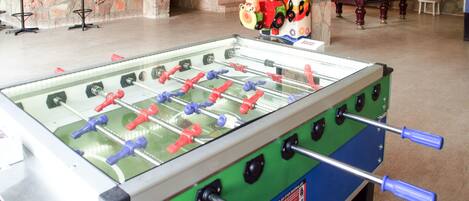 A foosball table in a room with a pool table, bar stools, and a decorative house model.