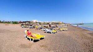 Een strand met ligbedden, parasols en een pier op de achtergrond.