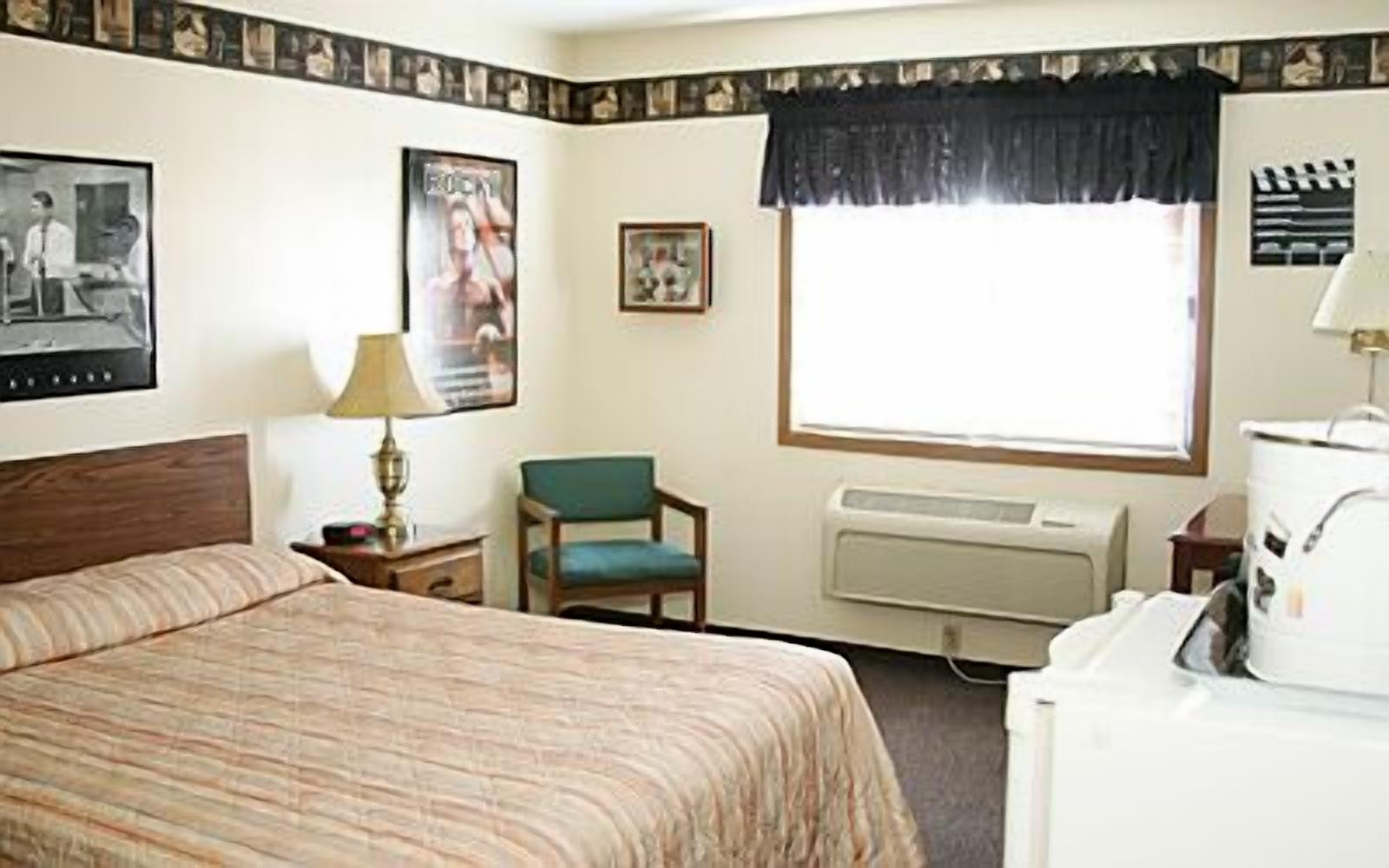 A hotel room with a bed, a chair, a desk, a lamp, a window, and a radiator.
