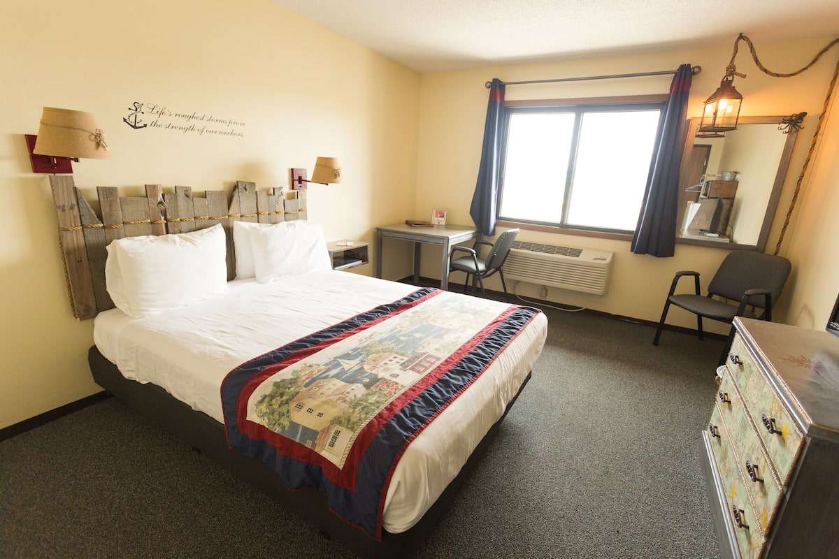 A hotel room with a bed, desk, chair, dresser, and a window with curtains.