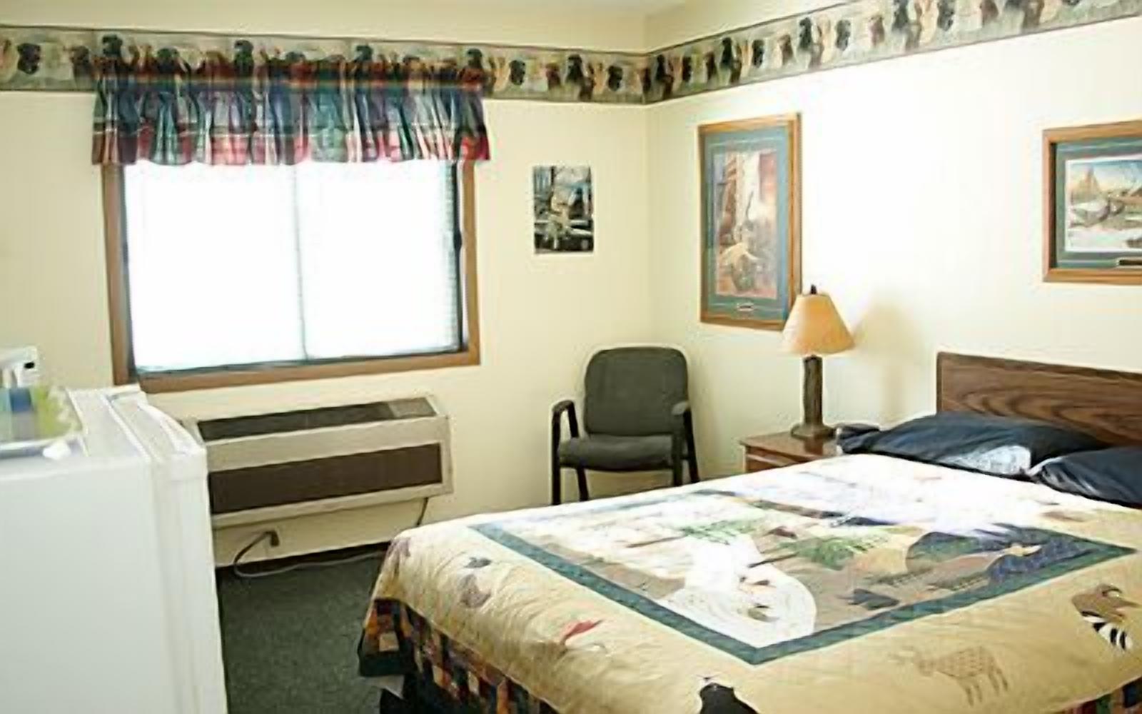 Habitación de hotel con cama, una silla, un escritorio, una l ámpara y ventana con cortinas.