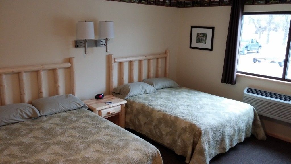 Une chambre avec deux lits, une table de chevet, une lampe, un tableau au mur et une fenêtre donnant sur l’extérieur.
