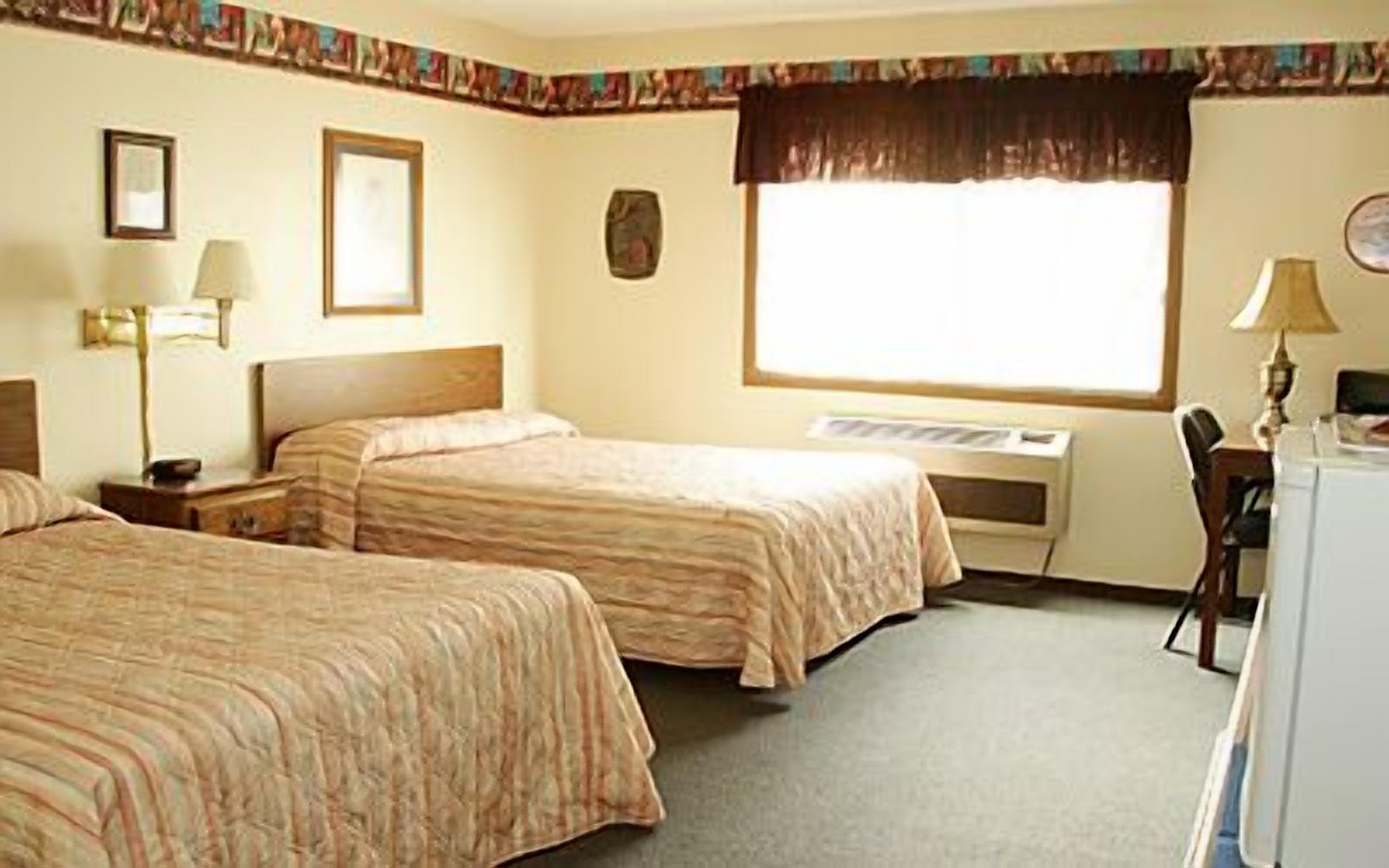A hotel room with two beds, a desk, a chair, a desk lamp, and a window with a curtain.