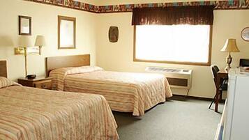 A hotel room with two beds, a desk, a chair, a desk lamp, and a window with a curtain.
