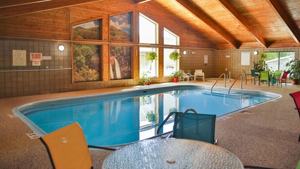 An indoor swimming pool with wooden ceiling beams, tiled walls, and a seating area with chairs and tables.