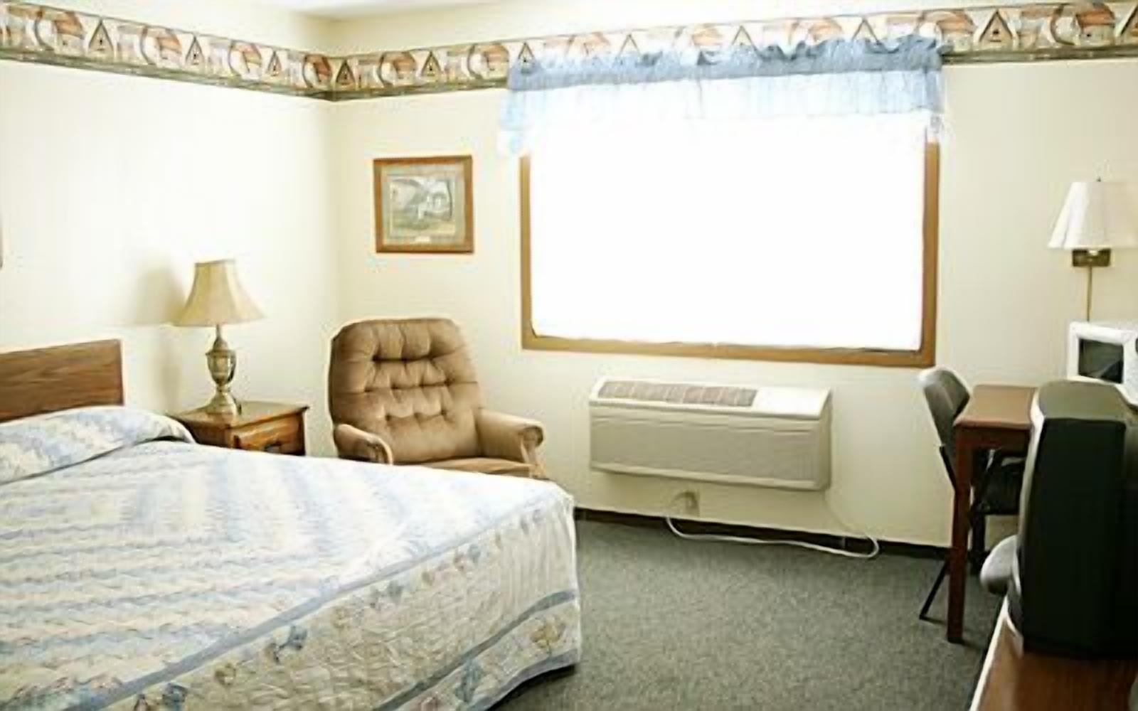 Une chambre d’hôtel équipée d’un lit, d’une chaise, d’un bureau, d’un climatiseur et d’une fenêtre avec un rideau.