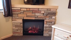 A fireplace with a stone facade, a television mounted above it, and a white dresser to the right.