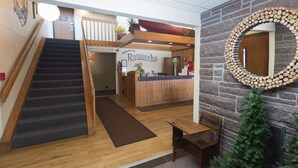 A reception area with a wooden staircase, a reception desk, a Christmas tree, and a stone wall with a circular mirror.