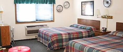 A motel room with two beds, a window with curtains, a microwave, a clock, and a wall-mounted lamp.