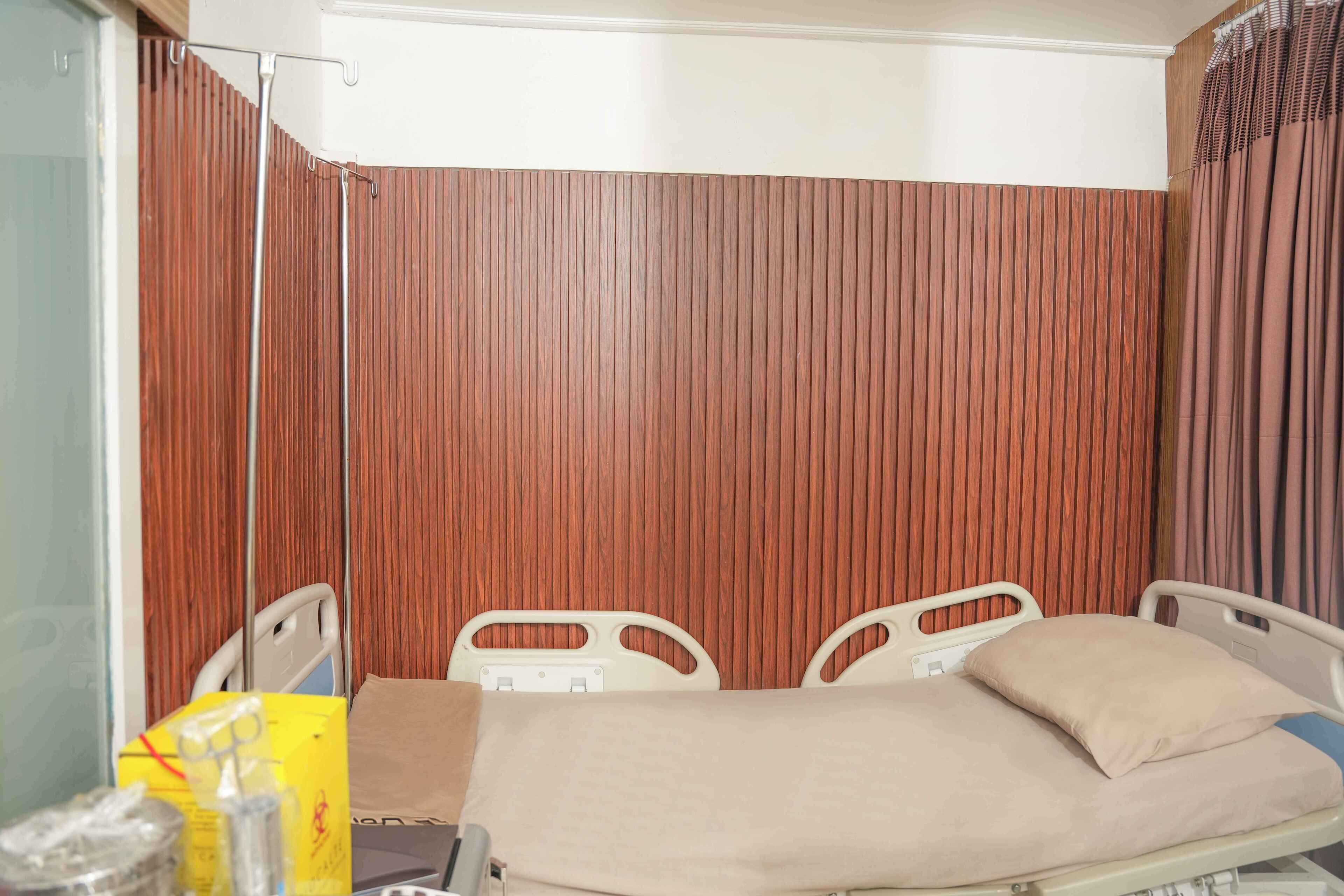 A hospital room with a bed, two chairs, a curtain, and a wooden panel wall.