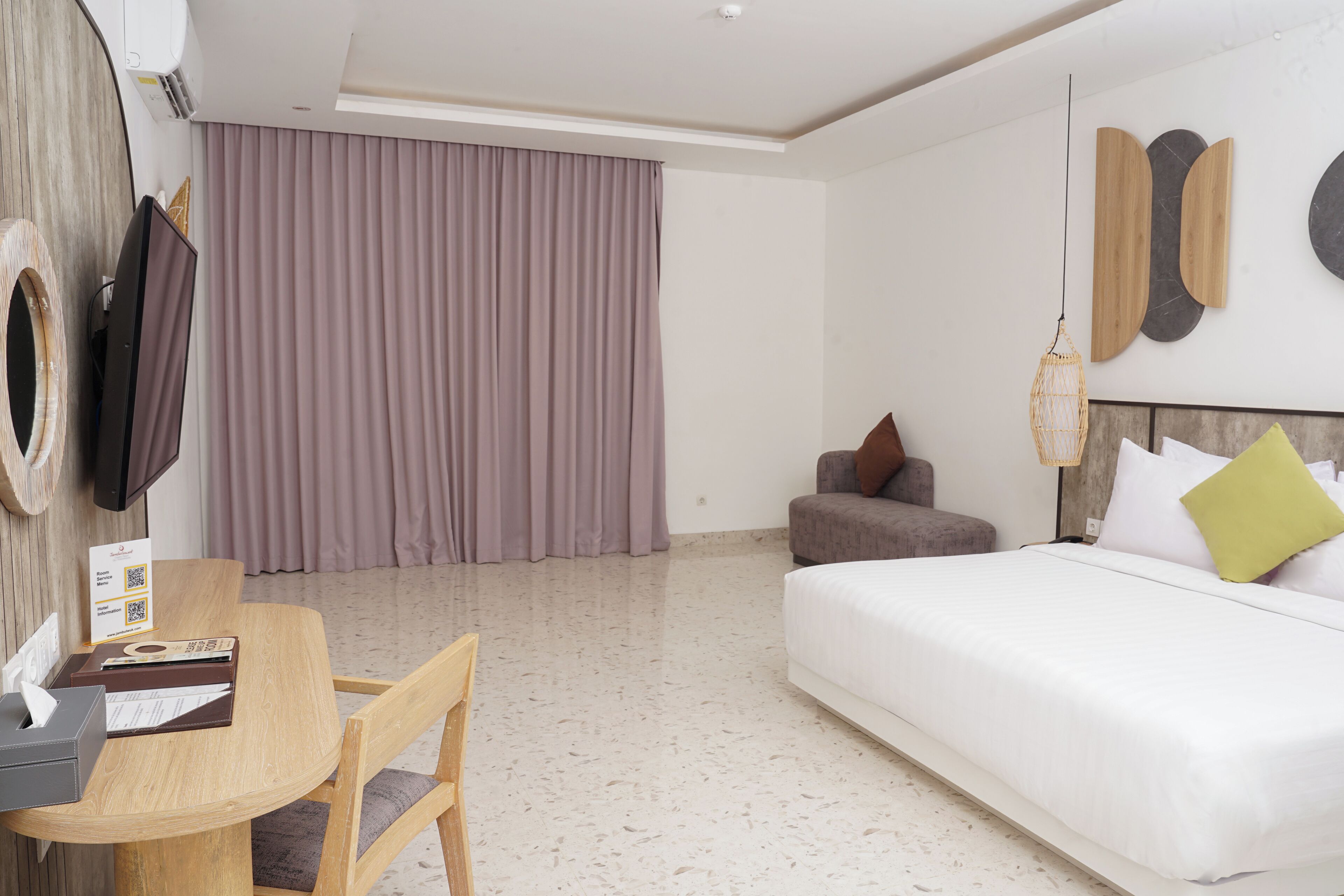 Hotelkamer met een bed, een bureau met stoel, een televisie en een groot raam met gordijnen.