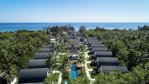A resort with multiple bungalow-style buildings arranged in a row, a central swimming pool, and a view of the ocean. - Jambuluwuk Oceano Resort Gili Trawangan (Gili Trawangan)