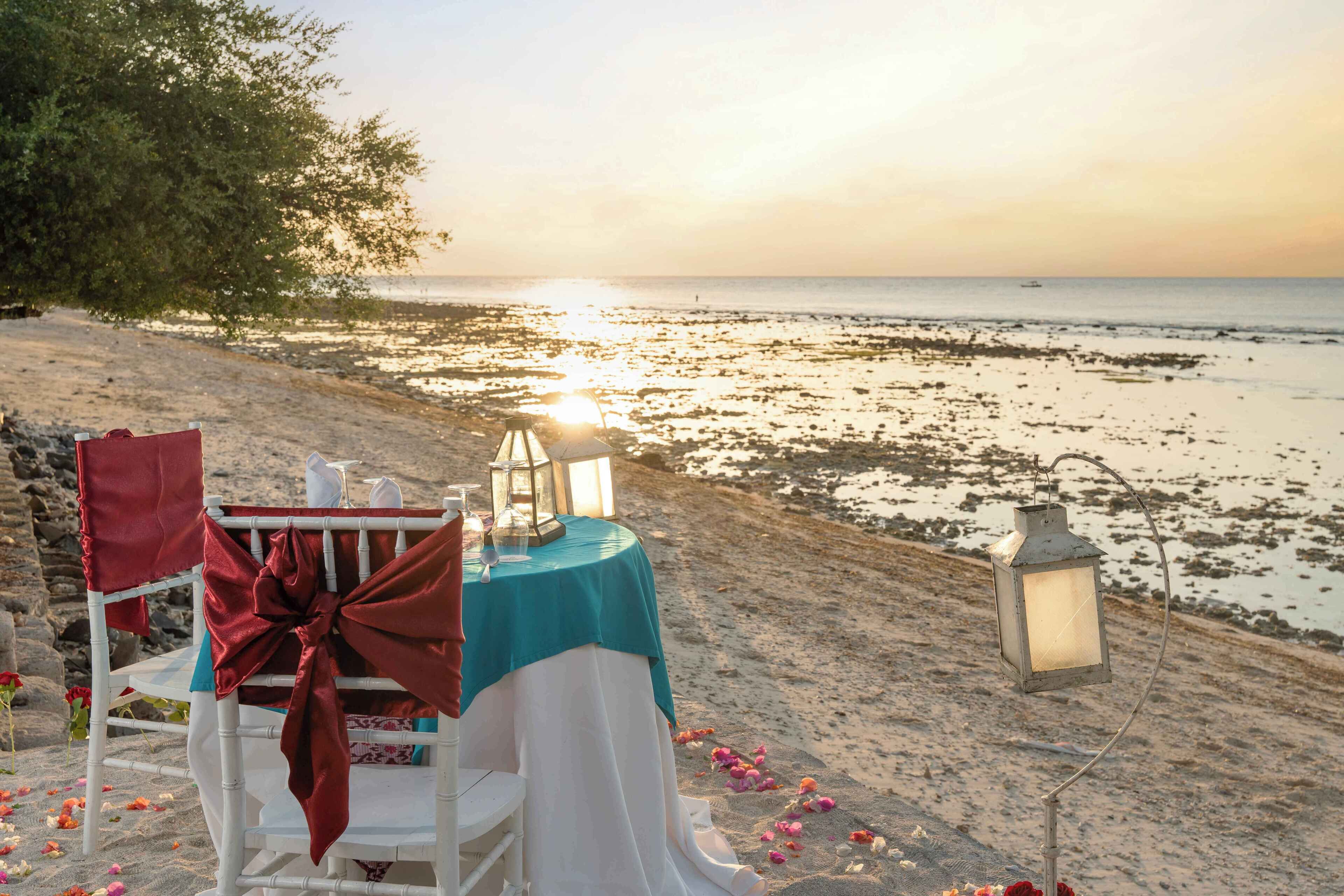 Mesa frente al mar, con mantel verde azulado, silla blanca y faroles.