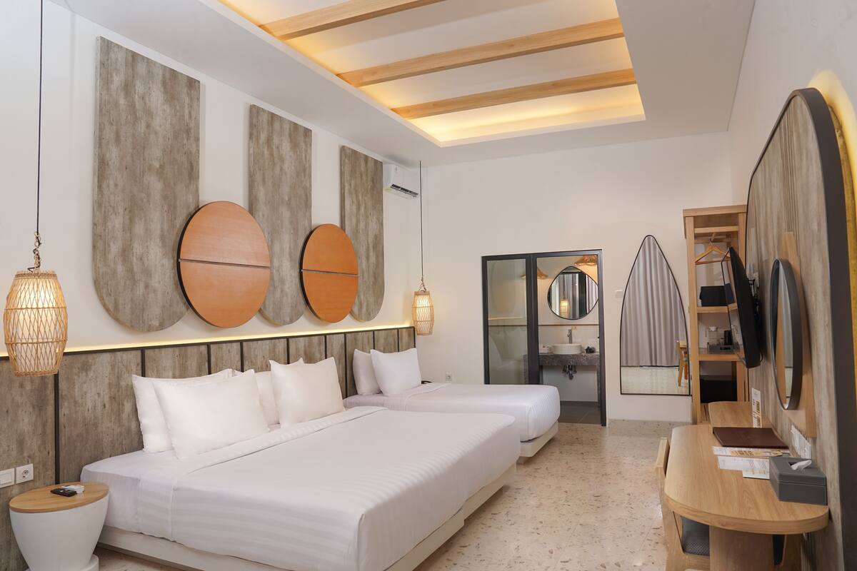 A modern hotel room with two beds, a wooden desk, a mirror, and a TV.