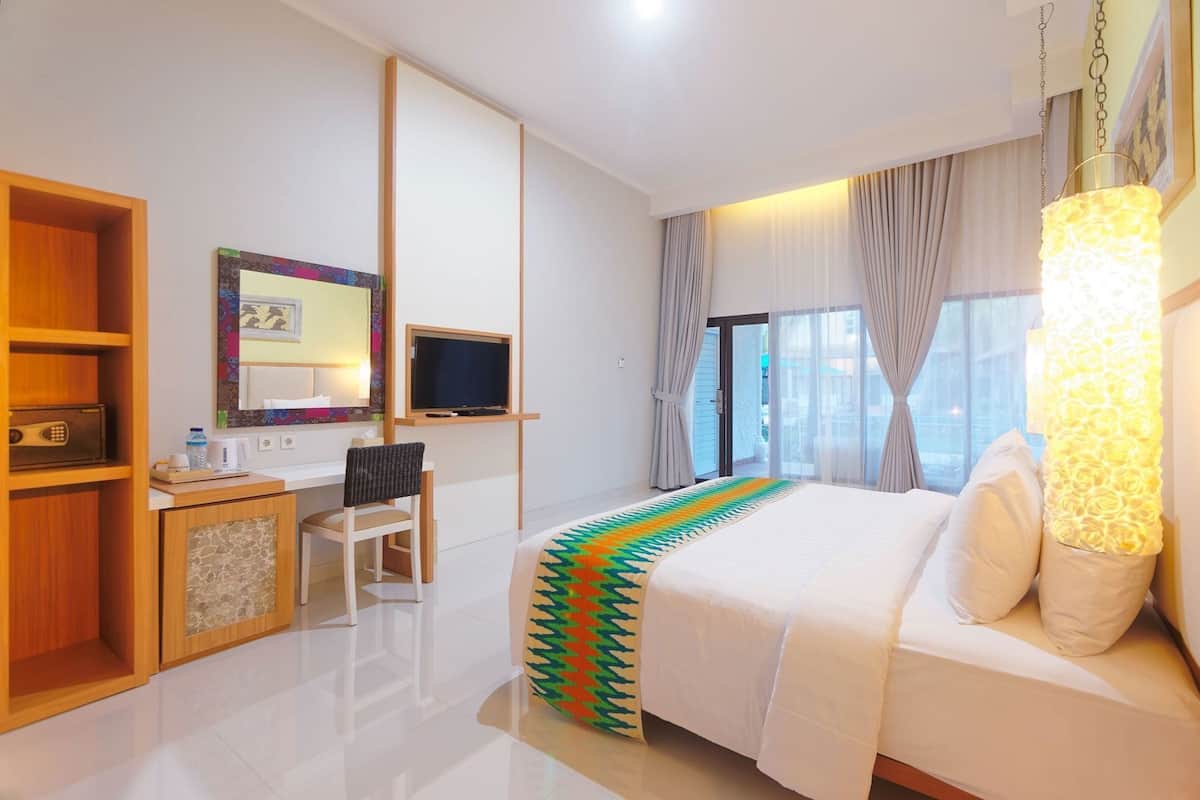A hotel room with a bed, a desk, a chair, a TV, and a window with curtains.