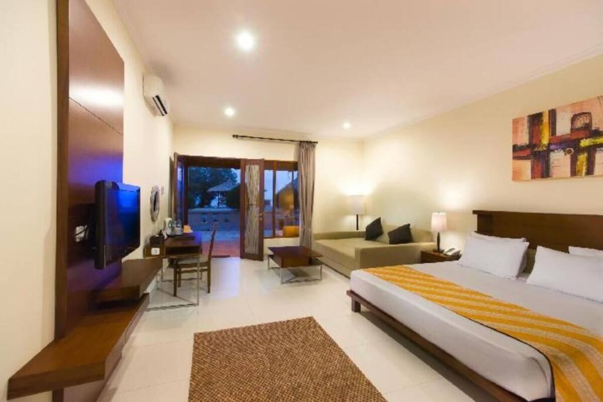 A hotel room with a bed, a TV, a desk, a chair, a lamp, and a painting on the wall.
