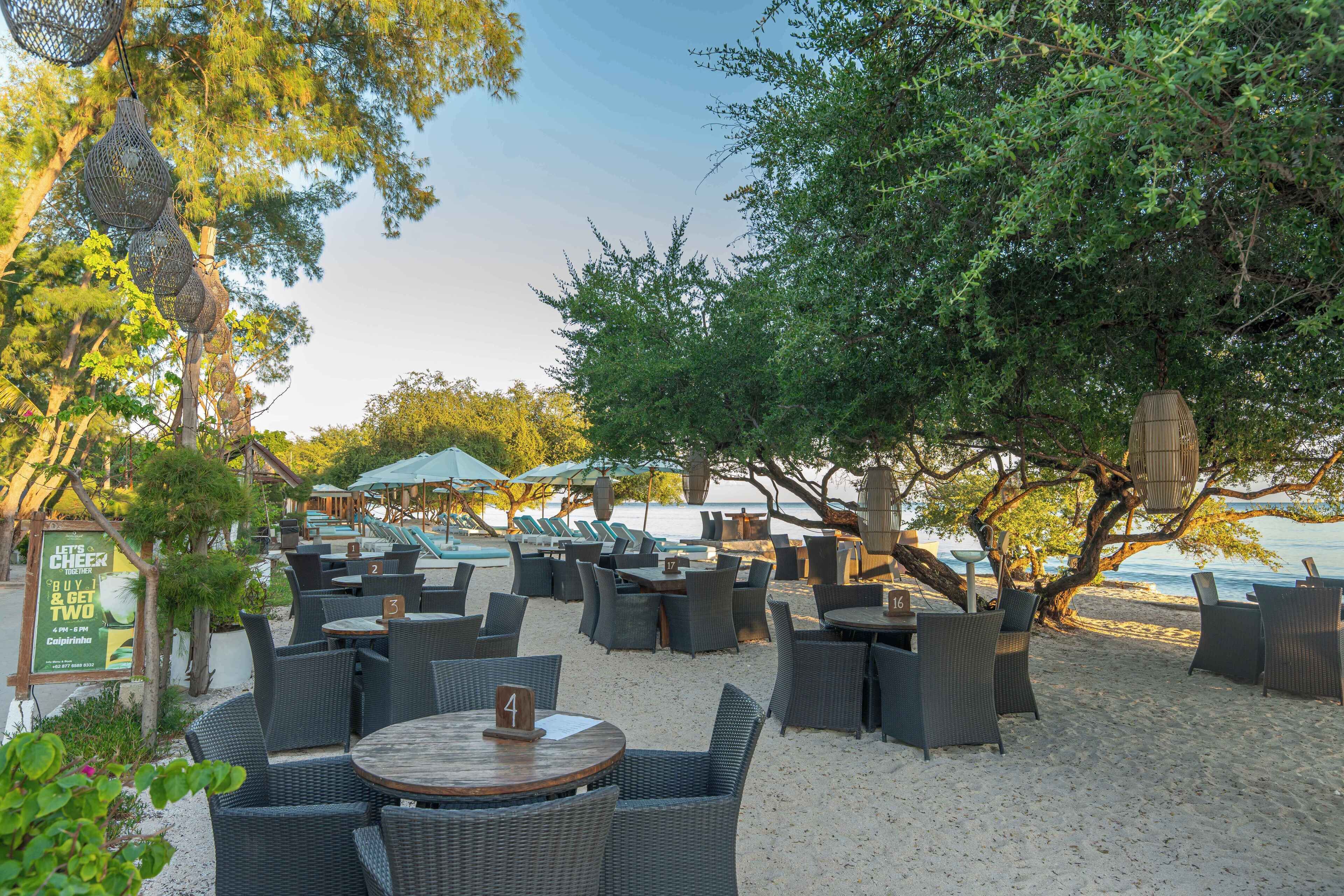 An outdoor seating area with wicker tables and chairs, umbrellas, and a view of the beach.