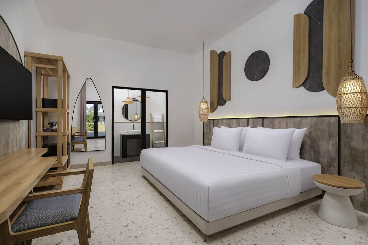 A modern hotel room with a large bed, wooden furniture, and a view through a glass door.