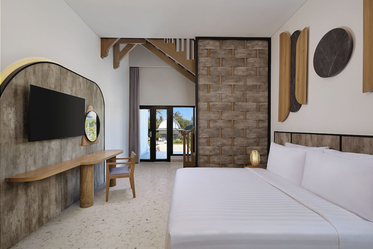 A modern hotel room with a large bed, a wooden bench, a flat-screen TV, and a stone accent wall.
