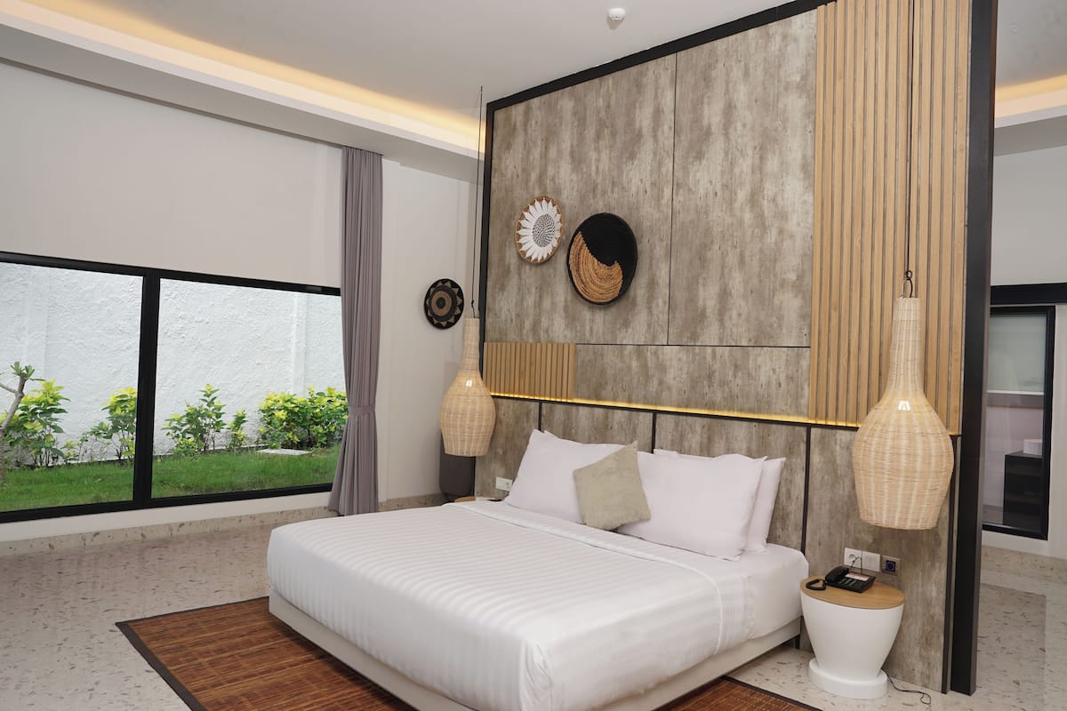 A modern bedroom with a large bed, a view of greenery outside, and a unique wall design.