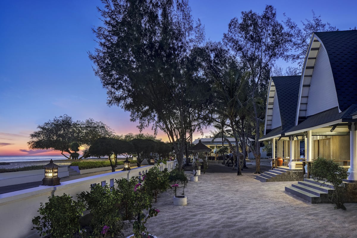 A beachfront hotel with a covered walkway, outdoor seating, and a view of the ocean at dusk.