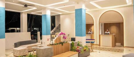 Een moderne lobby met een receptiebalie, een zithoek en een trap.