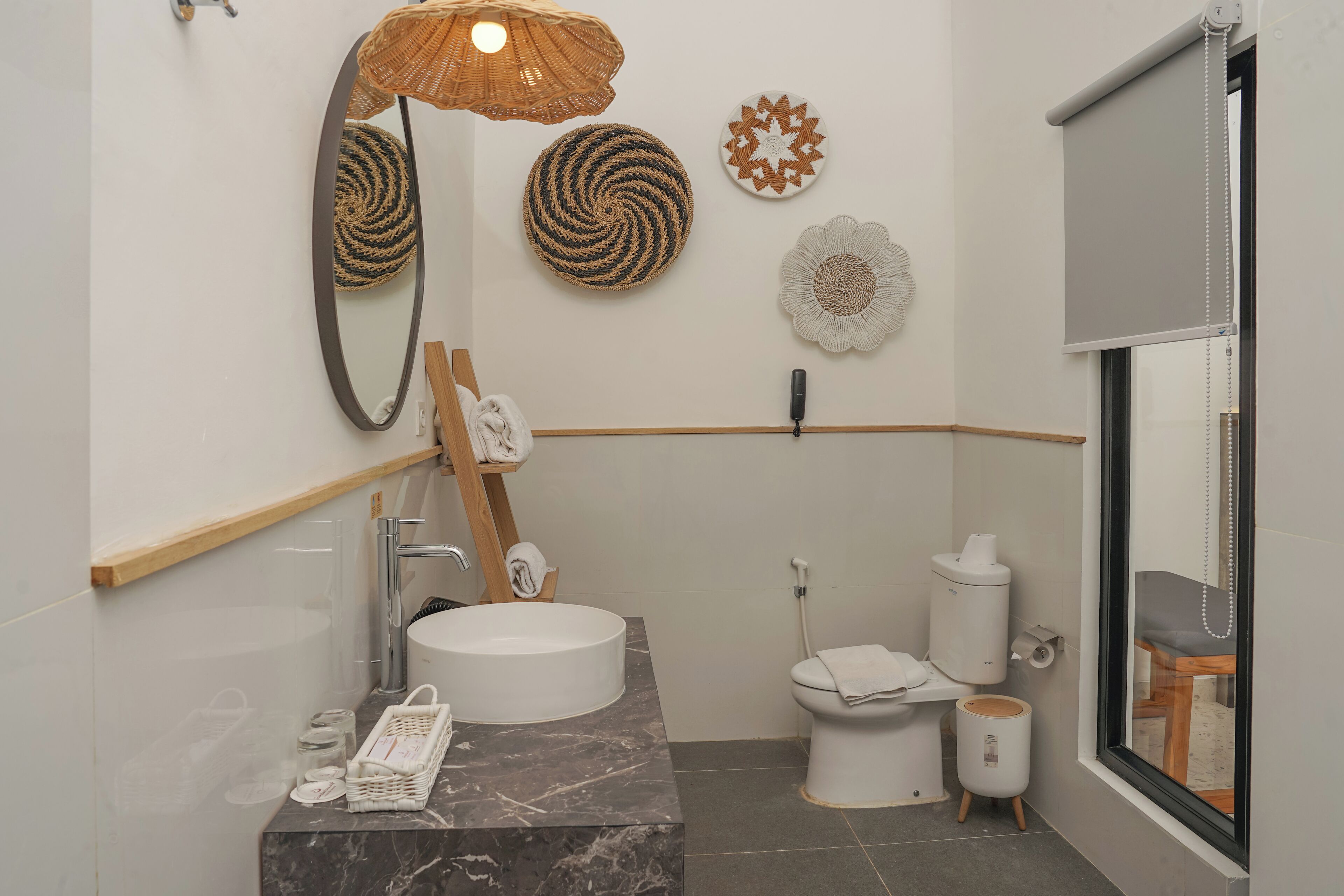 A modern bathroom with a round sink, a mirror, a towel rack, a toilet, and a window.