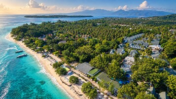 An aerial view of a coastal resort with beachfront properties, clear turquoise waters, and a backdrop of mountains.
