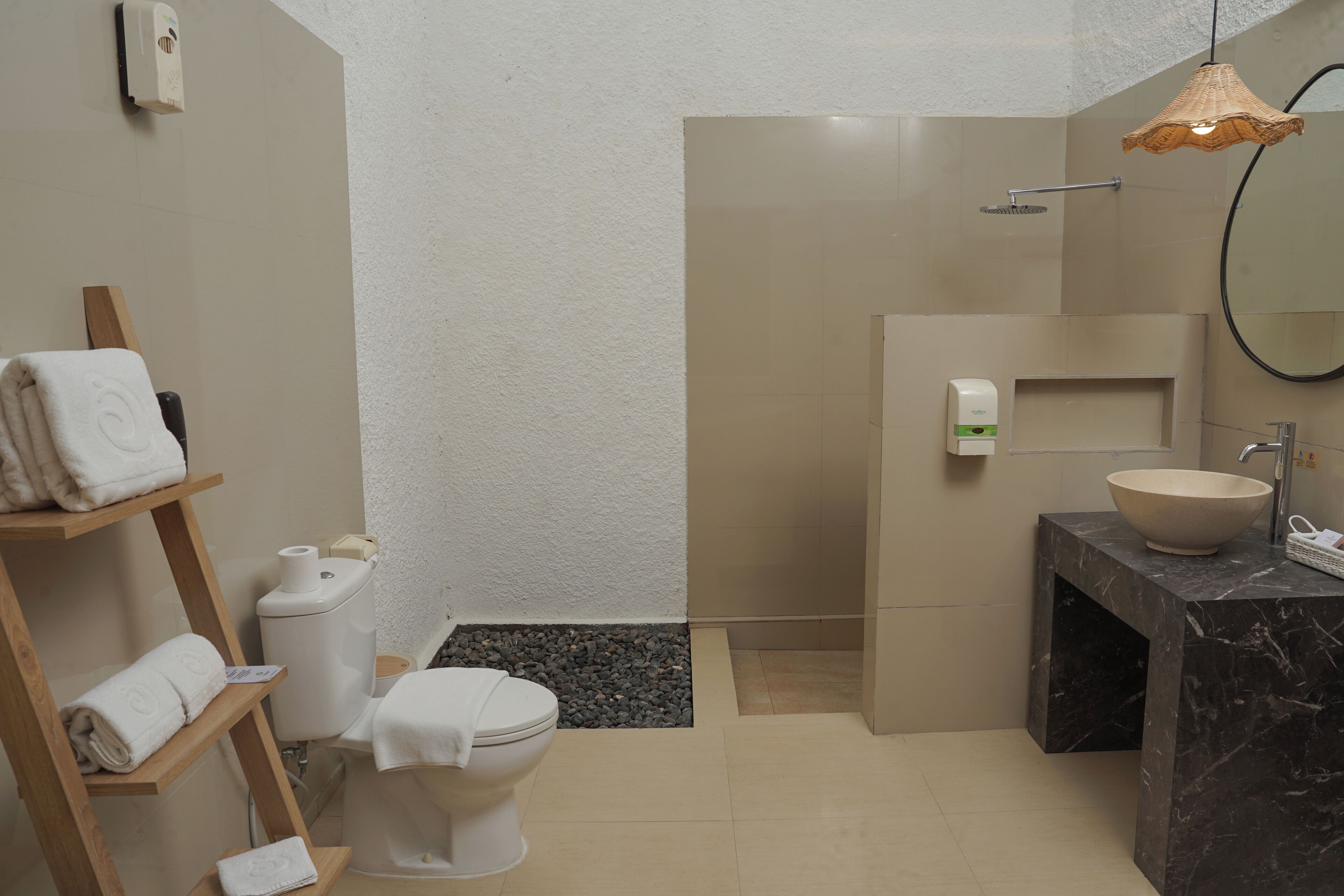 A bathroom with a toilet, a sink with a marble countertop, a shower, and a towel rack with folded towels.