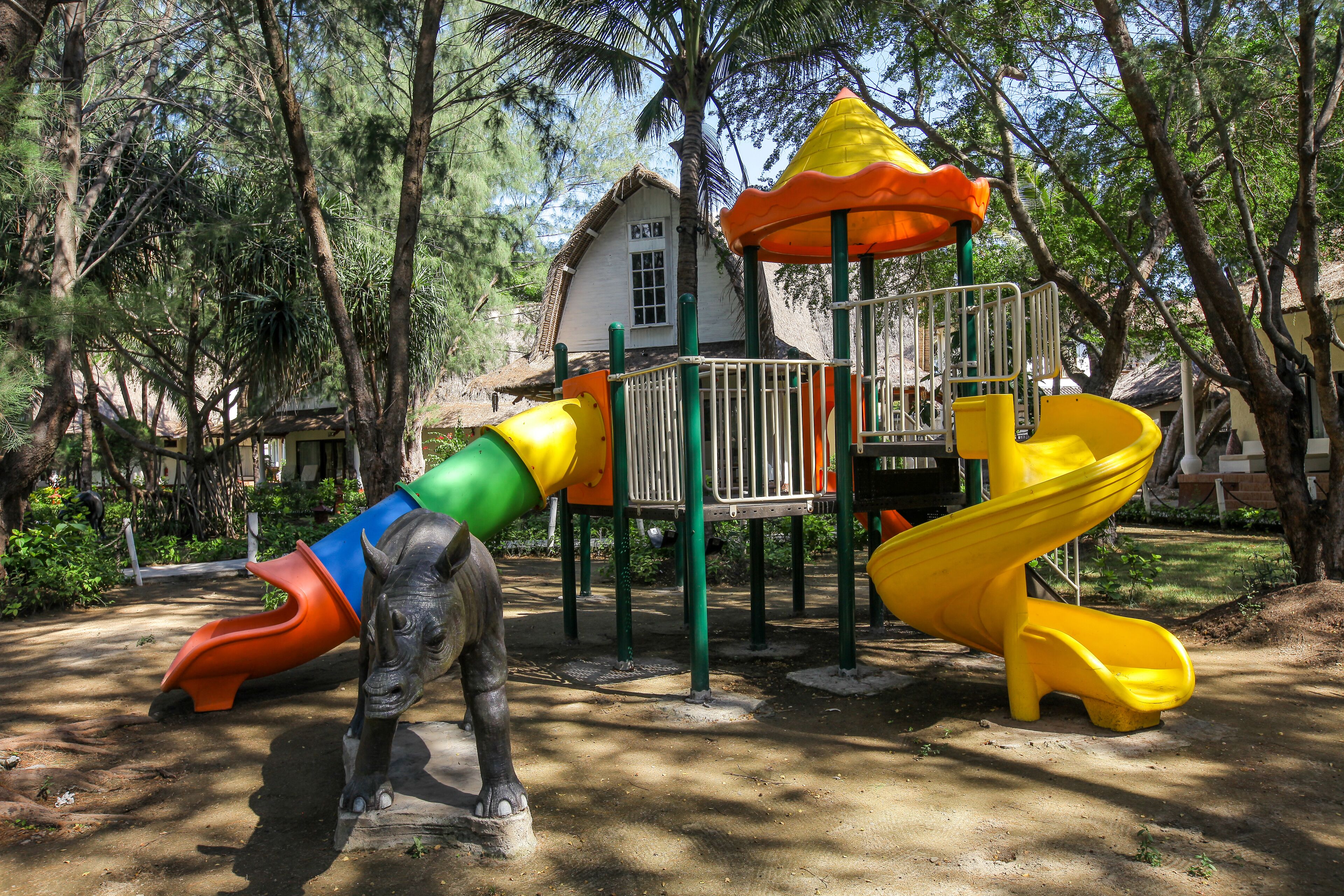 A playground with a slide, climbing structures, and a statue of a rhinoceros.