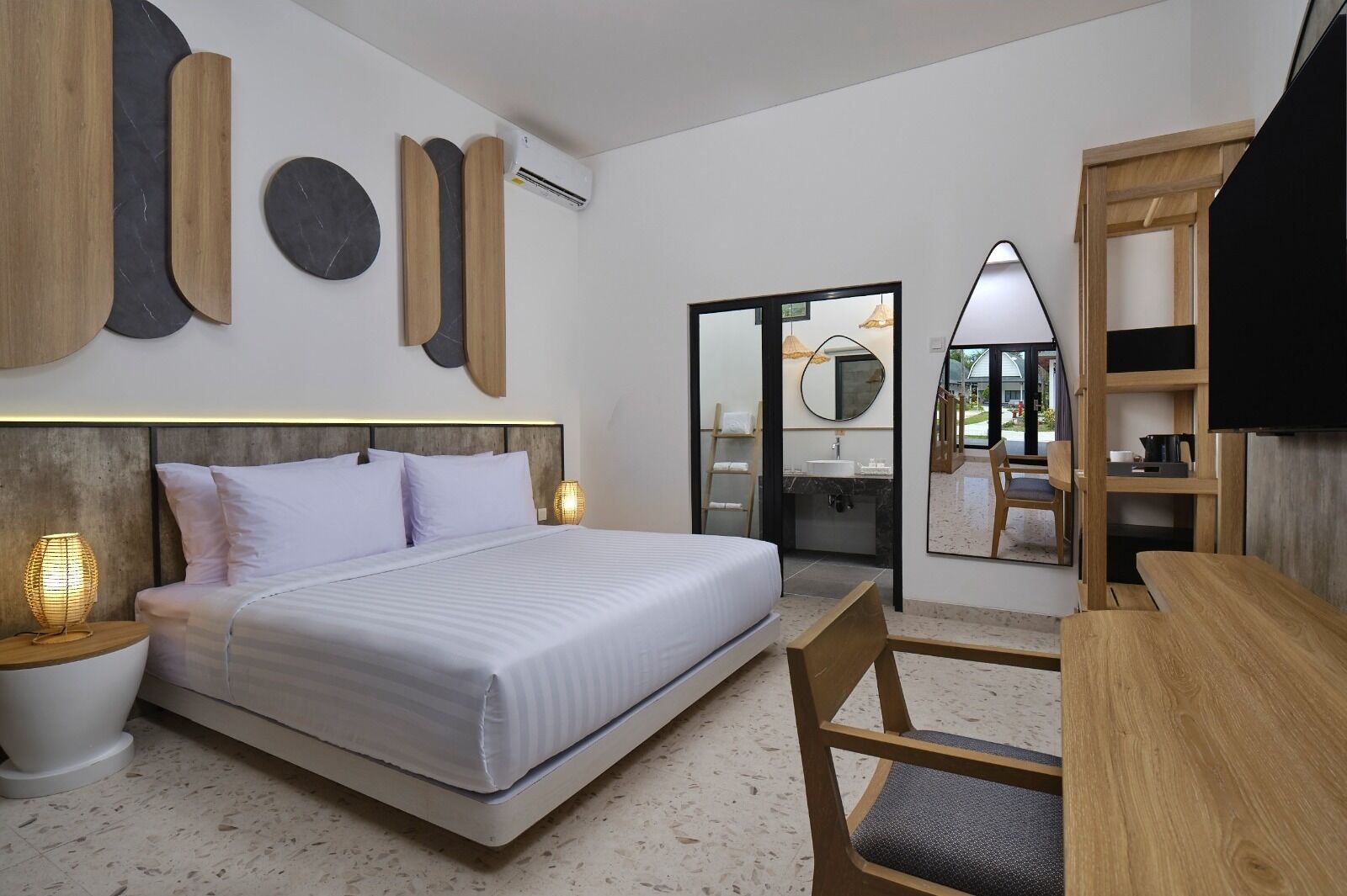 Una habitación de hotel moderna con una cama grande, lámparas de noche, una silla de madera, un escritorio y un televisor.