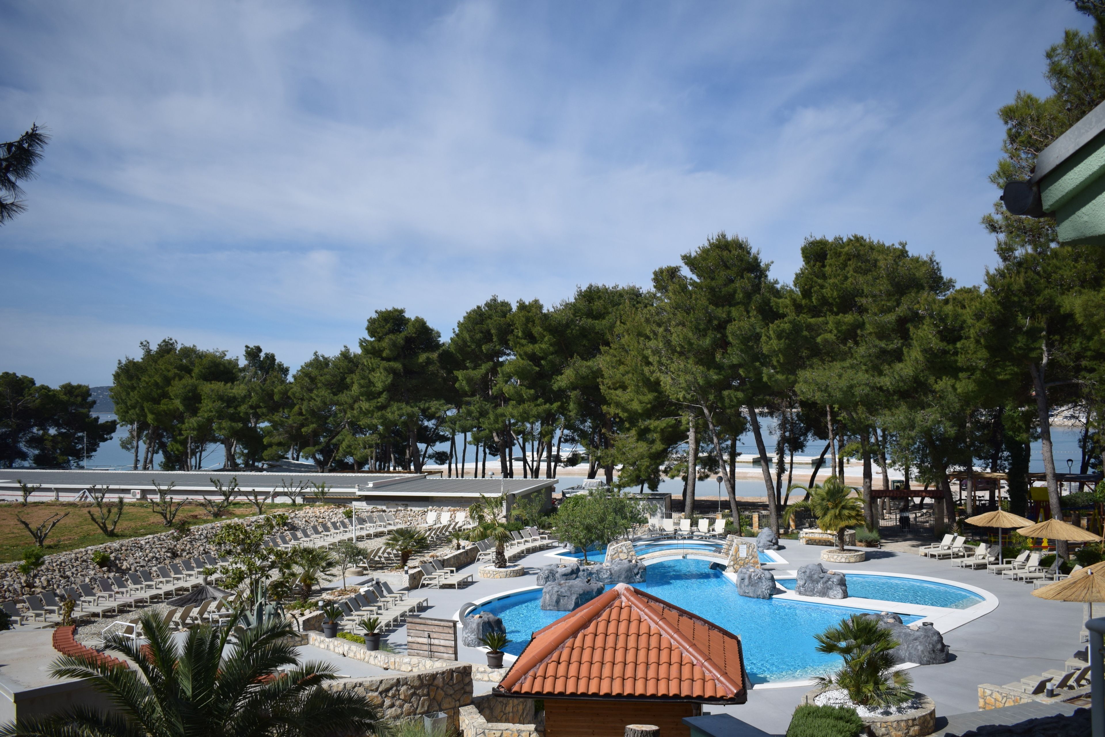A resort pool area with multiple lounge chairs and a central swimming pool surrounded by trees and a view of the sea.