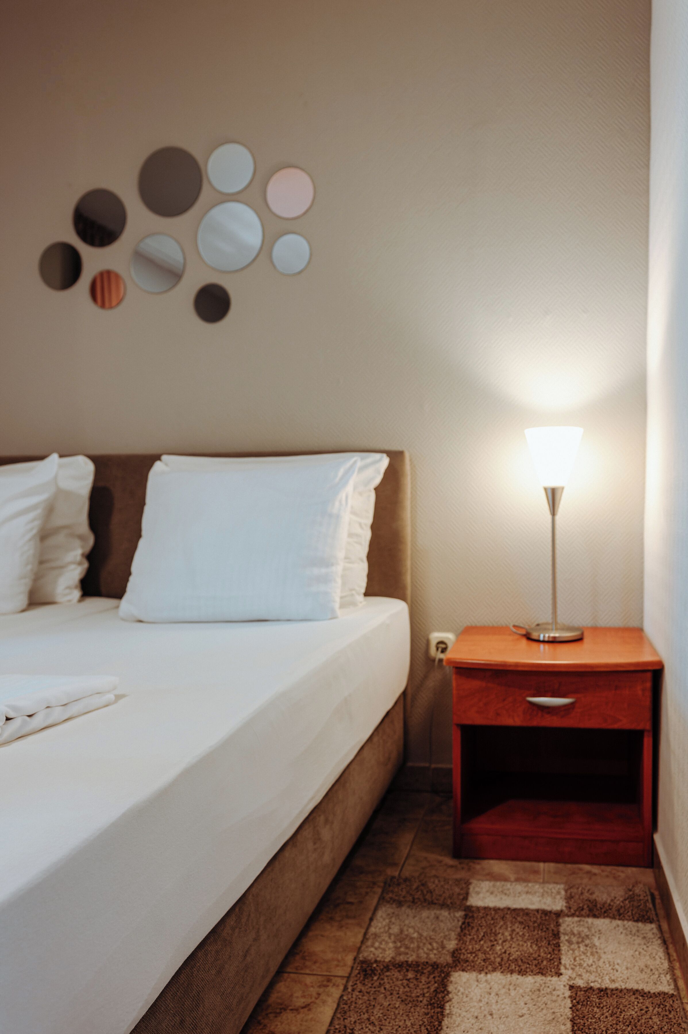 A hotel room with a bed, a nightstand with a lamp, and a wall-mounted mirror.