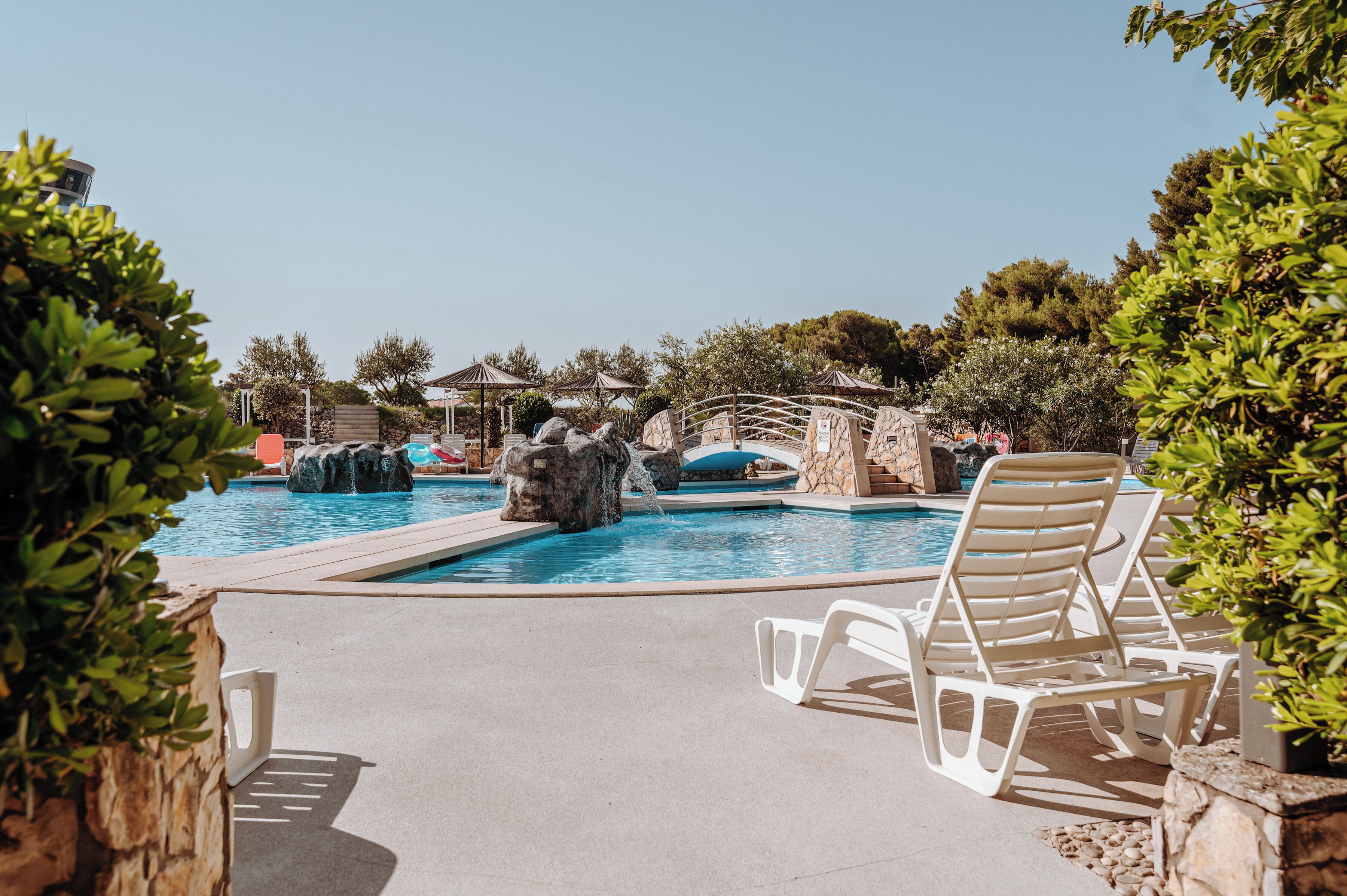 Un espace piscine agrémenté de chaises longues, d’un élément décoratif aquatique et d’une végétation luxuriante.