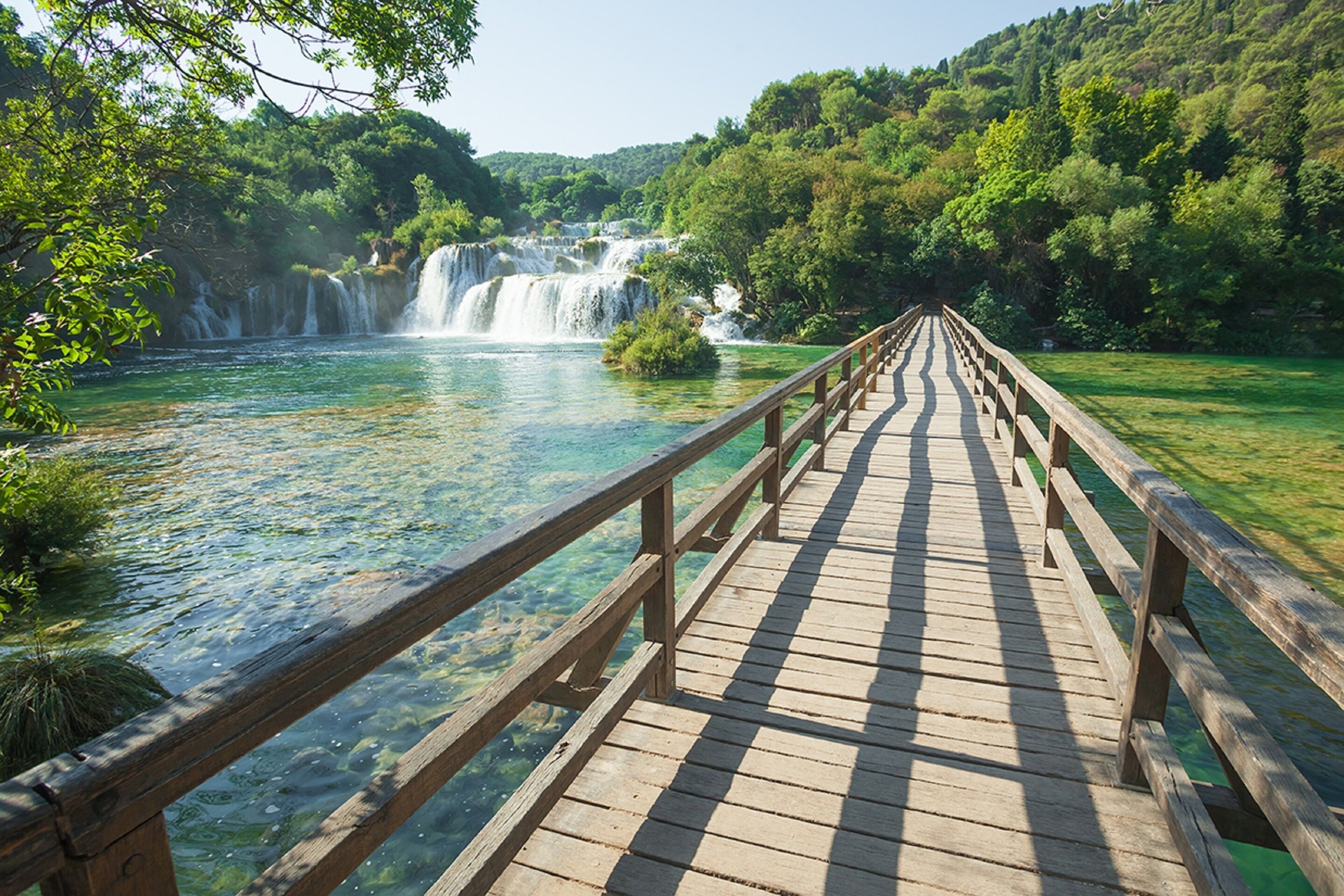 A wooden bridge leading to a waterfall surrounded by lush greenery.