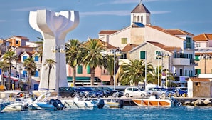 A coastal town with a prominent white sculpture, a church with a bell tower, and a marina with boats. - Matilde Beach Resort (Vodice)