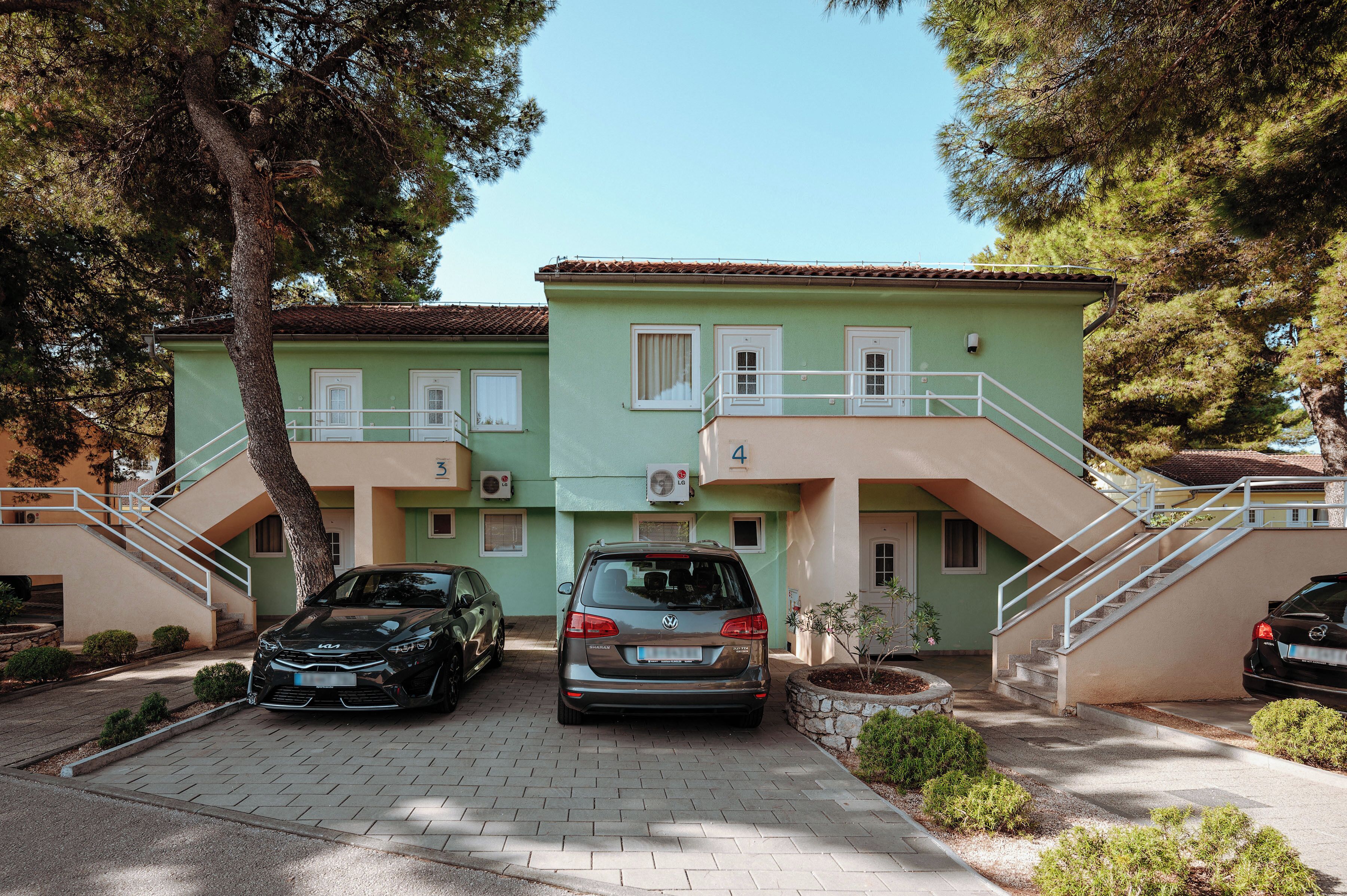 A two-story building with a green facade, two cars parked in front, and a staircase leading to the entrance.