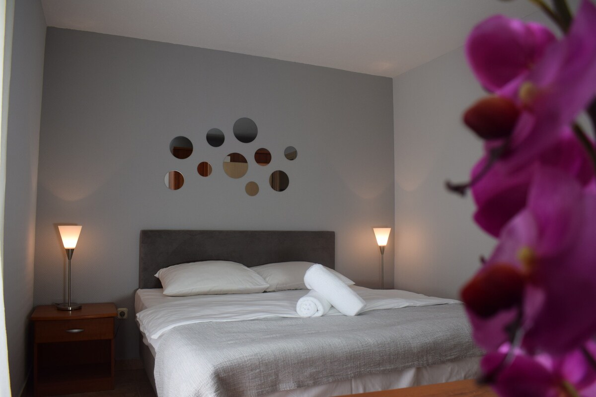 A neatly made bed with a grey headboard, two bedside lamps, and a wall with circular mirrors.