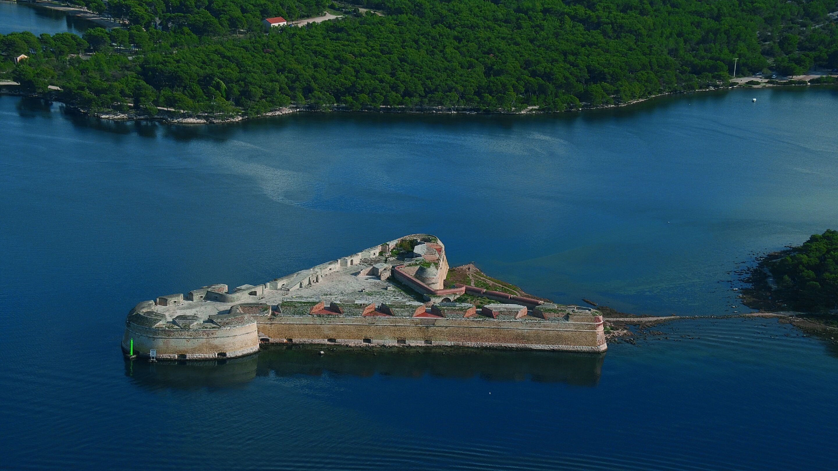 An aerial view of a historic fort surrounded by water, with a dense forest in the background.