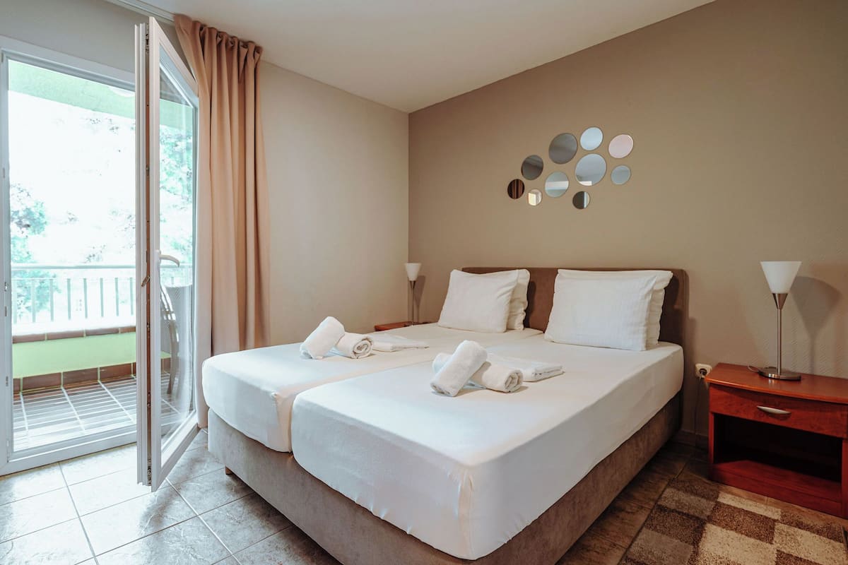 A hotel room with a large bed, two bedside tables, a wall-mounted mirror, and a sliding glass door leading to a balcony.