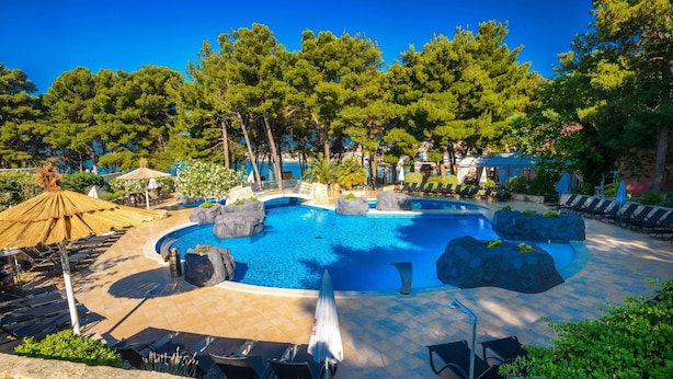 A pool area with lounge chairs, a hot tub, and a thatched umbrella. - Matilde Beach Resort (Vodice)