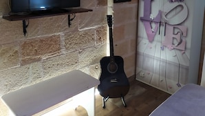 A room with a brick wall, a TV mounted on a shelf, a guitar, a bench, and a wardrobe with 'LOVE' decor. - A casa di Mich il Salento Lu sule Lu mare Lu ientu (Monteroni di Lecce)